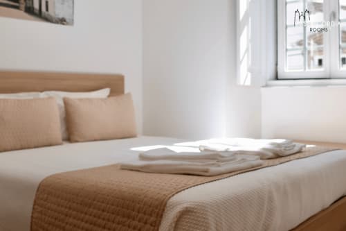 Quarto luminoso na SM Stays Collection em Guarda, Portugal, com roupa de cama creme, cabeceira de madeira e vistas da cidade
