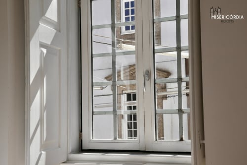 Quarto luminoso com portas francesas abertas mostrando vistas da cidade no hotel Misericórdia Rooms em Guarda, Portugal