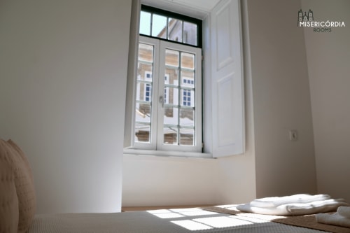 Quarto luminoso com grande janela vista para a cidade da Guarda, roupa de cama branca e decoração minimalista na SM Stays Collection