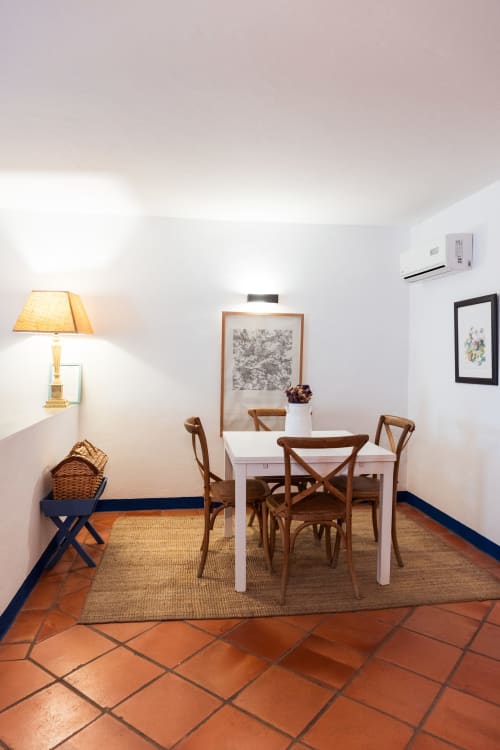 Área de jantar clara na villa Casas de Juromenha com mesa branca, cadeiras de madeira, pisos de terracota e iluminação quente