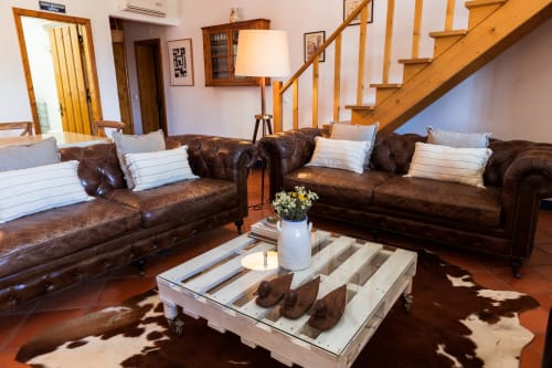 Elegante sala de estar na villa Casas de Juromenha com sofás de couro marrom, escada de madeira, lareira e almofadas listradas