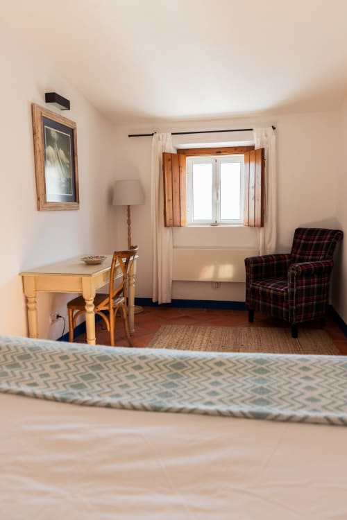 Quarto luminoso da villa em Casas de Juromenha com mesa de madeira, poltrona xadrez e vista para o jardim