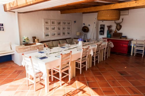 Espaçosa sala de jantar na villa Casas de Juromenha com cadeiras de madeira, mesa branca, vigas aparentes e piso de terracota
