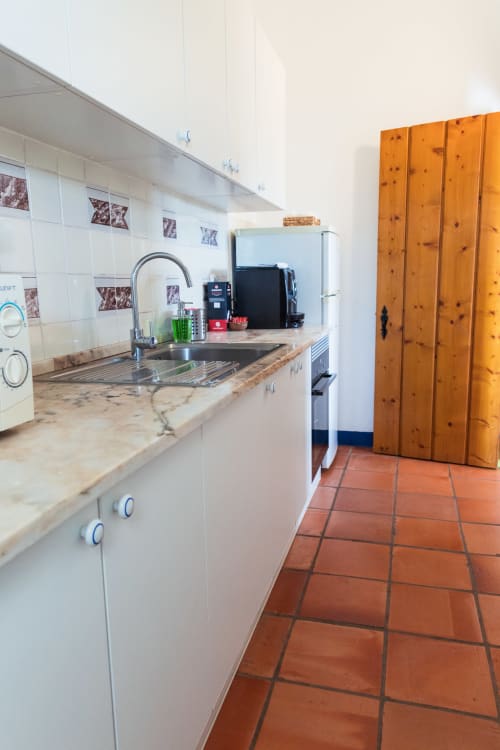 Cozinha da villa Casa 6 em Casas de Juromenha com armários brancos, bancada de mármore, pia, refrigerador e ladrilhos de terracota
