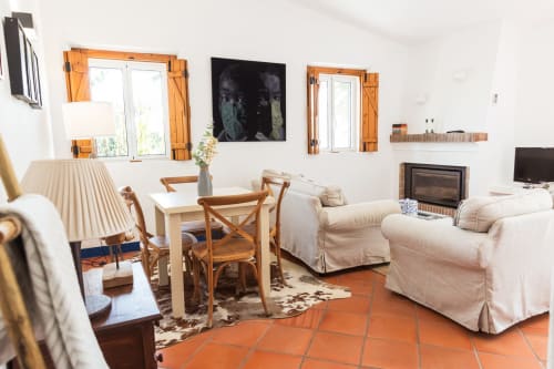 Área de estar clara na villa Casas de Juromenha com móveis creme, acabamentos em madeira, piso de terracota e vistas do jardim