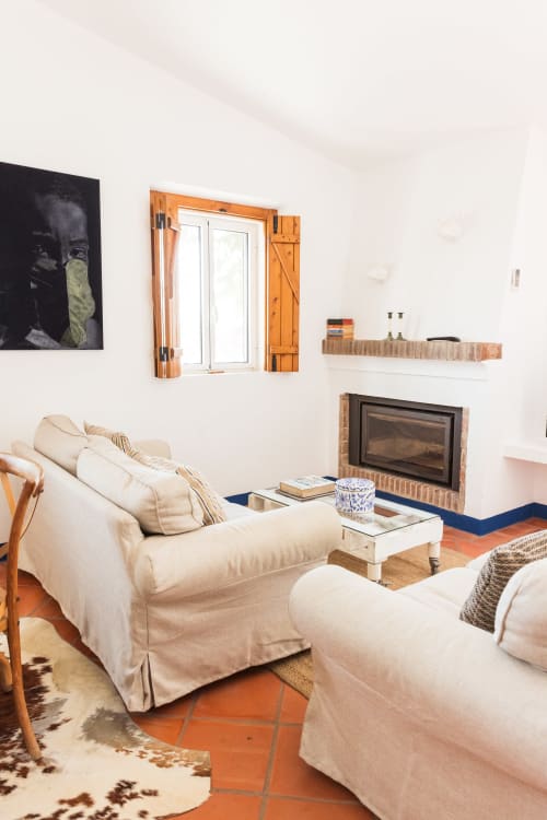 Sala de estar luminosa com sofás creme, lareira, venezianas de madeira e pisos de terracota na villa Casa 6 em Juromenha