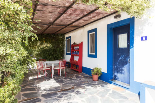 Pátio da Casa 6 na villa Casas de Juromenha com porta azul, acentos vermelhos, área de jantar e vegetação exuberante
