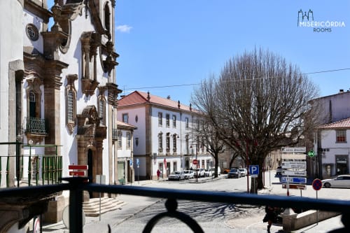 Praça histórica de Guarda com arquitetura colonial, fachada da igreja e carros estacionados sob céu azul