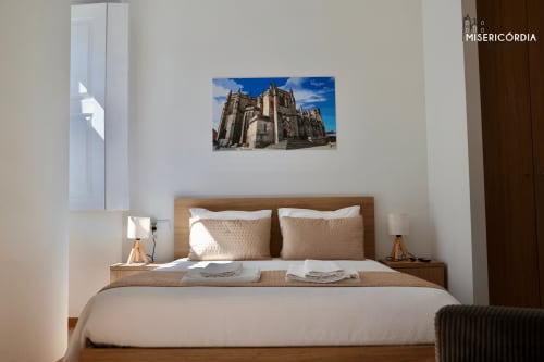 Quarto moderno na SM Stays Collection em Guarda com cama de madeira, roupa de cama bege e obra de arte religiosa acima