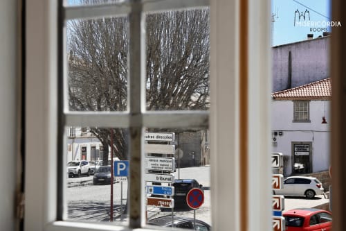 Vista da janela do quarto da Sé Catedral em Guarda mostrando praça de paralelepípedos, árvores nuas e placas de orientação