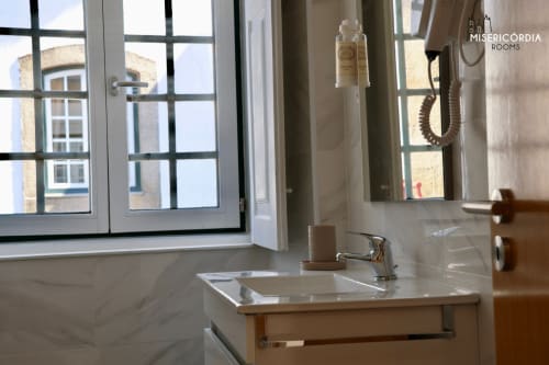 Casa de banho moderna em Misericórdia Rooms em Guarda com lavatório em mármore, grande espelho e vista da cidade através de janelas com grade