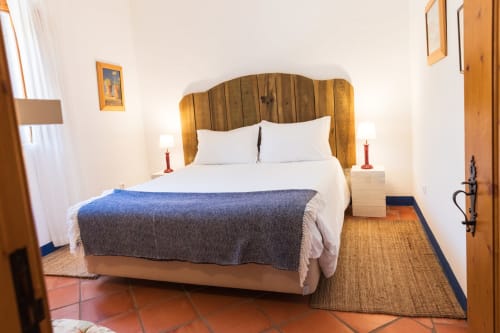 Cama com estrutura de madeira, almofadas brancas e manta azul em quarto iluminado da villa Casas de Juromenha, Juromenha Portugal