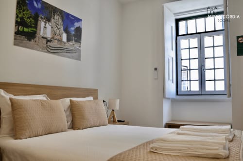 Quarto Alameda na SM Stays Collection Guarda com roupa de cama creme, cabeceira em madeira e vista da cidade através de grandes janelas