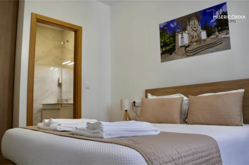 Quarto moderno da SM Stays Collection Guarda com cama queen, cabeceira em madeira, banheiro suite e fotografia com vista da cidade