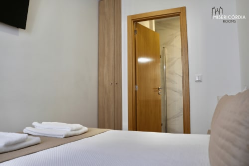 Quarto moderno na SM Stays Collection Guarda com porta de madeira, roupa de cama branca e móveis contemporâneos