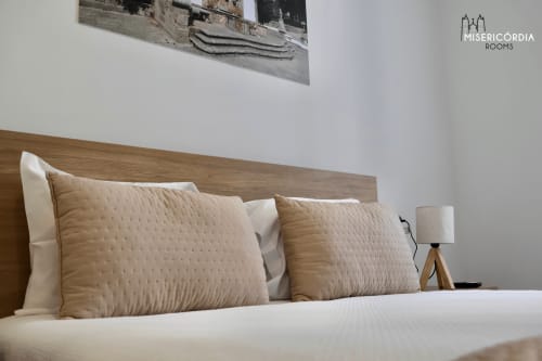 Quarto aconchegante na Misericórdia Rooms em Guarda com cabeceira de madeira, almofadas acolchoadas bege, roupa de cama branca e luminária de cabeceira