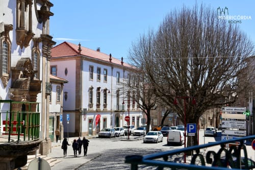 Edifício histórico rosa e branco em Guarda, Portugal com carros estacionados, árvores nuas e plaza em pedra - vista da cidade por SM Stays