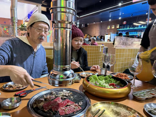 Family dining at Korean BBQ restaurant with tabletop grill and fresh ingredients
