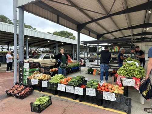 Farmers market with fresh vegetables and produce at outdoor stall under metal roof structure