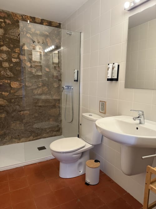 Modern bathroom at Mas Ribas Hotel in Palamos with walk-in shower, white sink, toilet and terracotta tile floor