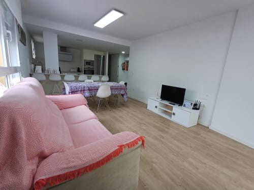 Spacious open-plan living area in Algemesi apartment with pink sofa, dining table, kitchen, and TV setup