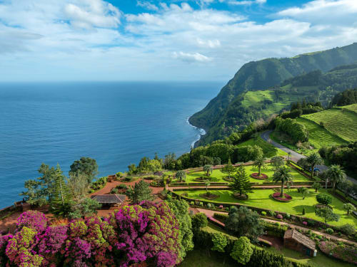 Golden Mermaid Villa Portugal overlooks lush gardens, magenta flowers, and dramatic coastal cliffs above turquoise ocean