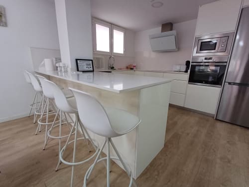 Modern white kitchen with island seating, stainless steel appliances, and wooden floors at Algemesi Home apartment in