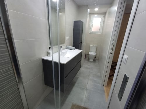 Modern bathroom at Algemesi Home with black vanity, white sink, glass shower enclosure, and white tile walls