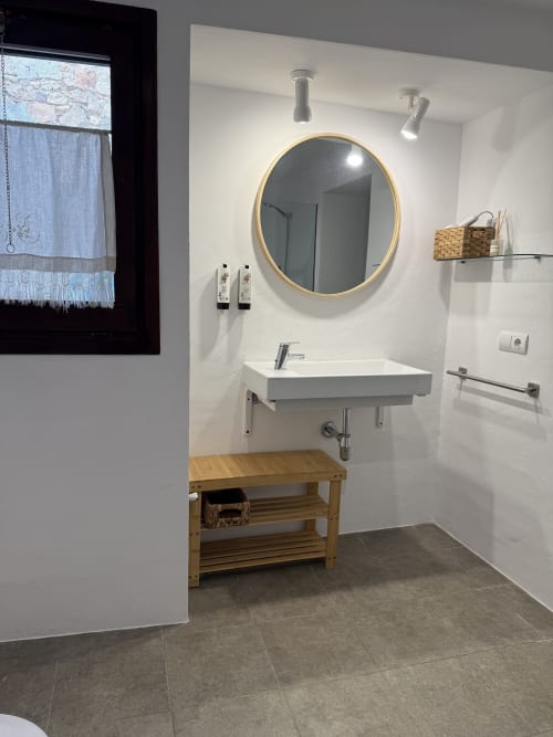 Modern bathroom at Mas Ribas Hotel in Palamos with round gold mirror, white sink, wooden vanity, and grey tile floor