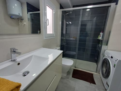 Modern bathroom in Algemesí Home apartment with white sink, toilet, black tile shower, washing machine, and heated towel rack
