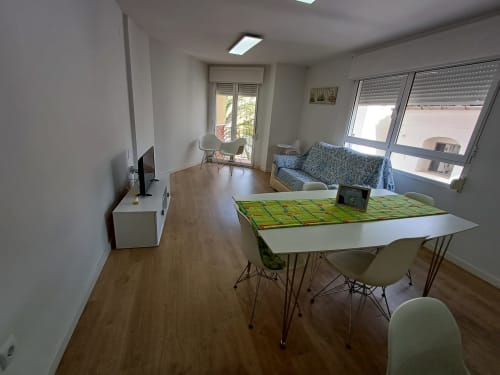 Modern apartment living room at Algemesi Home with dining table, sofa, TV, and city views through windows