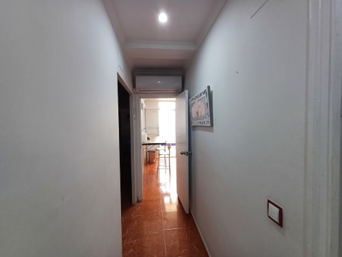 Couloir étroit de l'appartement Algemesi Home aux murs blancs, carrelage en terre cuite et porte ouverte sur le séjour