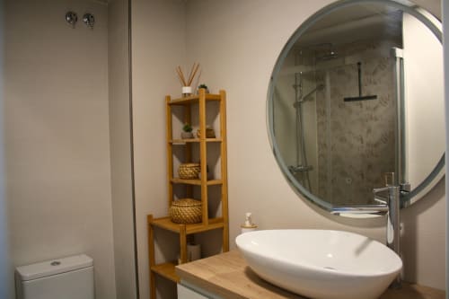 Baño moderno con lavabo vessel blanco, espejo redondo, estantería de madera y ducha en el apartamento Love Rent4 Málaga