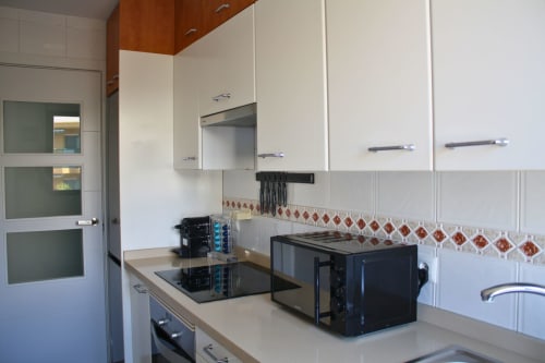 Cocina moderna con gabinetes blancos, estufa negra y azulejos decorativos en apartamento de Torremolinos