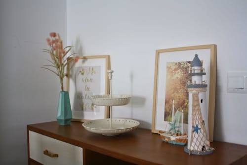 Decoración costera: jarrón turquesa con flores, arte enmarcado de faro, cuencos decorativos en cómoda de madera