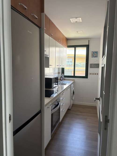 Cocina moderna en apartamento Love Rent4 Málaga con armarios blancos, electrodomésticos de acero inoxidable y vistas al mar
