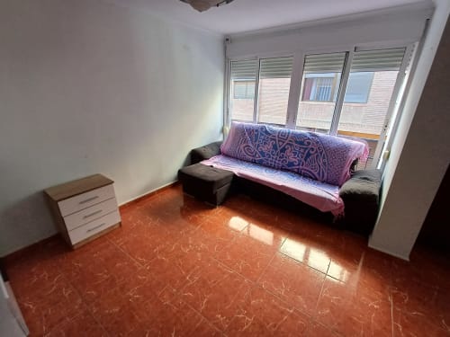 Salon lumineux de l'appartement Algemesi Home en Espagne avec canapé noir, coussins rose, carrelage rouge et vue sur la ville