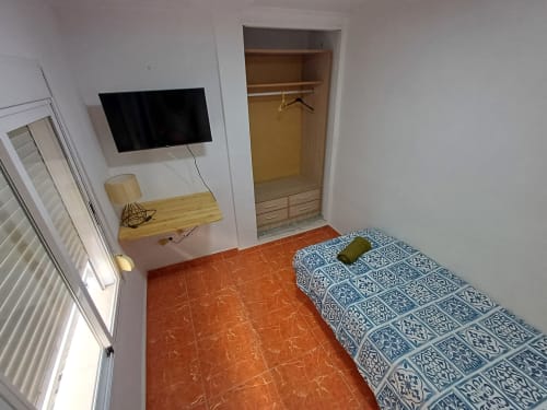 Chambre de l'appartement Algemesi Home avec lit, télévision, bureau en bois, placard et sol en carrelage terre cuite