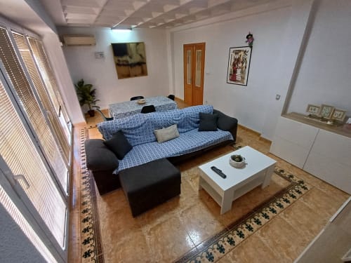 Sala de dia clara a apartament d'Algemesí amb sofà blau estampat, butaca negra, taula de centre blanca i vistes a la ciutat