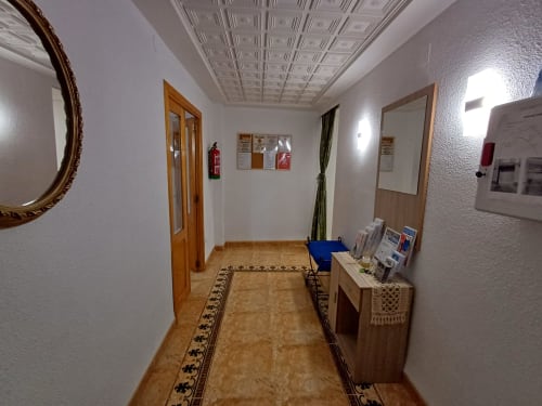 Passadís de l'apartament d'Algemesí amb portes de fusta, mirall decoratiu, sòl de rajoles, extintor i taulells d'avisos