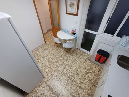 Cuina moderna amb electrodomèstics blancs, petita taula menjadora i paviment de teula de terracota en apartament d'Algemesi