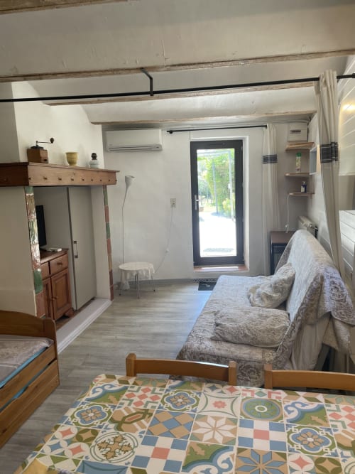 Intérieur du cottage La Maisonnette avec canapé, mobilier en bois, tapis motifs et porte vue jardin aux Gîtes du Mas Gibert
