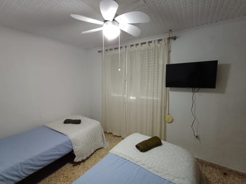 Dos llits individuals amb roba blanca en una habitació clara d'un apartament a Algemesi amb ventilador de sostre i televisor muntat a la paret