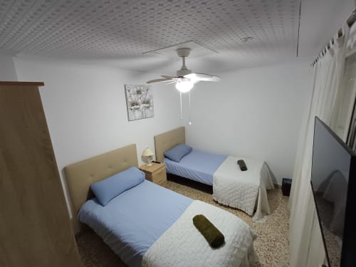 Habitació doble en apartament d'Algemesí amb roba de llit blava, ventilador de sostre i parets blanques