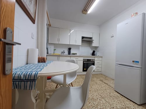 Cuina moderna i menjador a l'apartament d'Algemesí amb armaris blancs, electrodomèstics d'acer inoxidable i taula rodona