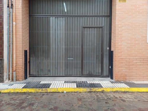 Porta de garatge de metall fosc amb vorera groga a l'entrada de l'edifici Algemesi Home a Espanya