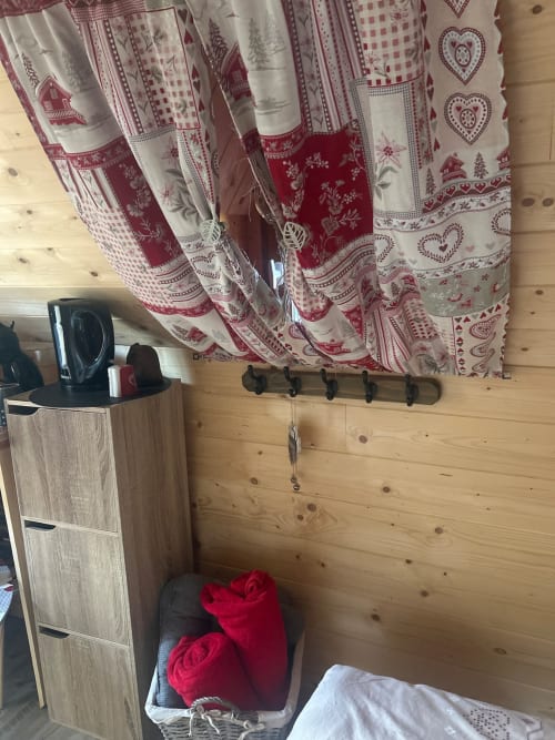 Intérieur cosy du cottage Les Cabanes des Marchous avec rideaux à motifs rouges et crème, murs en bois, patères et boiseries