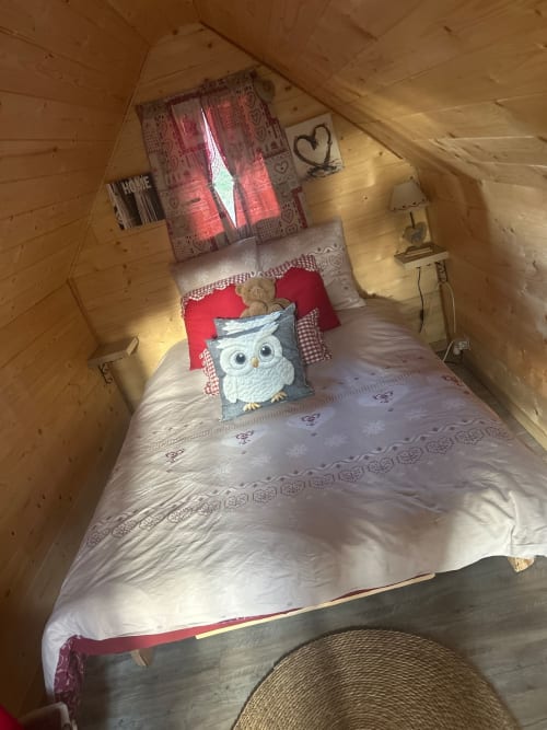 Chambre douillette en bois aux Cabanes des Marchous avec lit simple, oreiller chouette et décor rustique