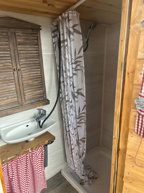 Salle de bain compacte de la Cabane Chouette avec lavabo, rideau de douche à motifs de feuilles et serviette rayée rouge aux Cabanes