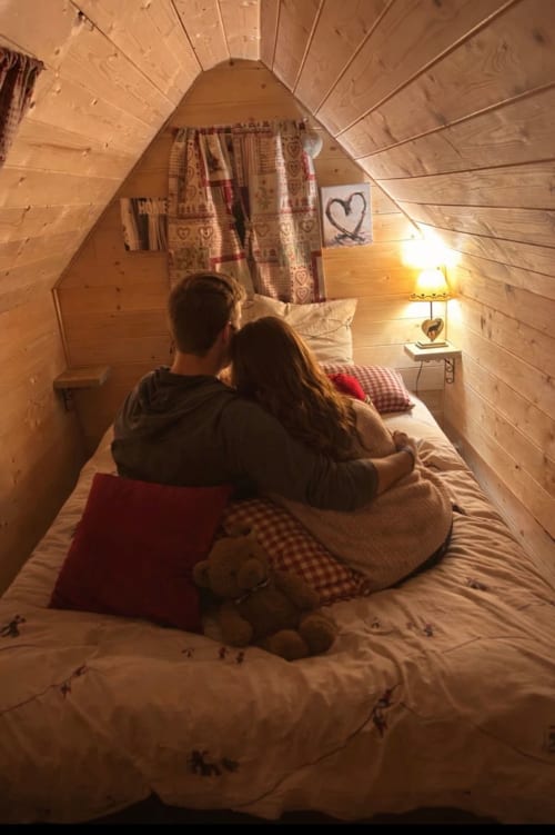 Couple se détendant sur le lit d'une cabane en bois cosy aux Cabanes des Marchous, Granges-Aumontzey